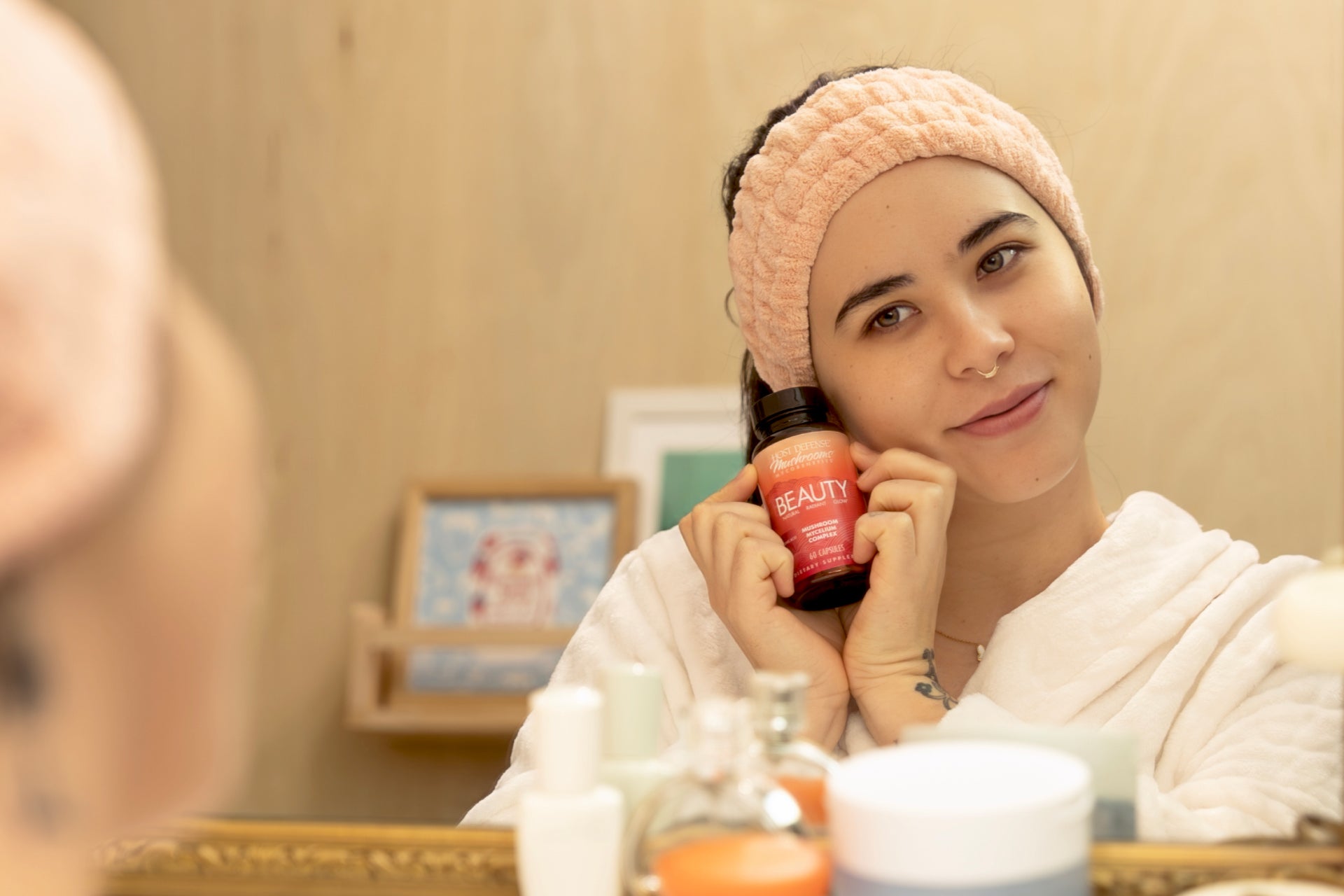 Women smiles while holding a bottle of MycoBenefits™ Beauty in front of a vanity mirror.